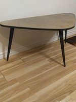 Side view of triangular solid wood coffee table with rounded corners and black tapered legs on hardwood floor.