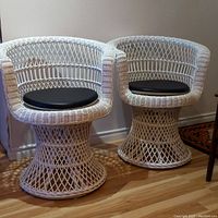 Pair of white painted vintage wicker swivel chairs with black cushions, showing overall design and condition.