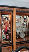 Full view of china cabinet content showing geisha doll, glassware, plates, and figurines on glass shelves with mirrored back