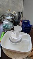 Wide view showing the white CorningWare baking dish, glass colander, ball jar, blue plastic containers, thermos, and other kitchen items