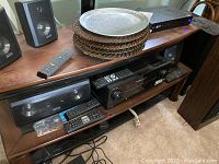 Photo of Pioneer receiver and two black speakers, remote control visible, placed on wooden shelving unit