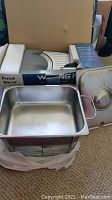 Photo showing Waring Pro food slicer partially visible in original box with foam inserts and stainless steel chafing dish pan with lid and metal handles.