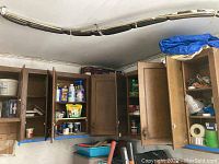 Garage cabinets with multiple shelves containing assorted chemicals, sprays, and various bottles including wood finish and bug control sprays.