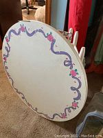 Photo of the oval white painted child’s table showing purple ribbon and pink rose painted border design.