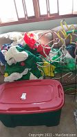 Image showing assorted folded inflatable Christmas decorations inside near windows with a red and green storage bin in front