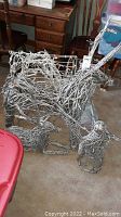 Two large lighted metal wire reindeer figures standing on carpet indoors, showing size and detailing.