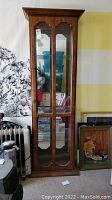 Front view of a tall wooden curio cabinet with glass-front doors, glass shelves, and mirrors inside. Photos taken to depict overall condition and structure.