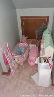 Photo showing pink Disney Princess crib with matching doll highchair, Barbie boat and sparkling pink decorative tree beside collapsible dollhouse.