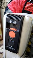 Close-up image of a Delonghi electric heater showing brand label, orange temperature dial, and switches