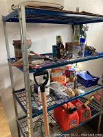 Side angle photo showing three of the five blue wire mesh shelves loaded with various household items, including paint cans, tools, garden hose and containers.