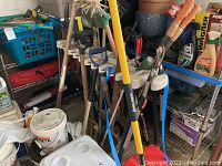 Photo of blue framed metal shelving rack holding various items including tools, detergents, and containers. Shows shelving structure and signs of scrap/cosmetic wear.