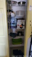 Closet shelving with various kitchen and household items including linens, cookware, bakeware in box, and more.