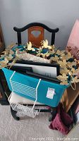 Lot of metal wall hangings, sea shell mirror, and picture frames in a turquoise box on black wood chair