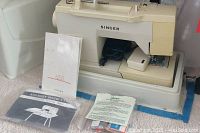 Singer sewing machine on hard plastic case with manuals and accessories arranged around it.