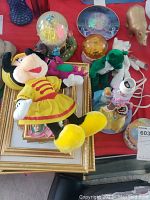 Top view of Minnie Mouse plush in yellow and red laying on gold photo frames with Disney snowglobes nearby