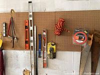 Photo of various hand tools hung on pegboard including levels, crowbar, rope, and measuring tape.