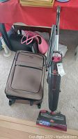 Photo showing Bissell Steam & Sweep Pet upright vacuum cleaner alongside brown wheeled suitcase and black and pink luggage bags on carpet.