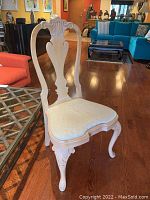 Side angle view showing the carved backrest, upholstery, and shape of seat and legs.