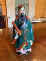Front view of the hand-painted ceramic figurine showing man with green robe, red scroll, and detailed facial features.