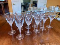 Ten clear crystal wine glasses arranged in two rows on a wooden table with background showing household items.
