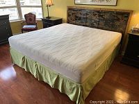 Full view of king size bed with light green bed skirt and white Dormeo Octaspring mattress, set against vintage headboard.