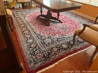 Full view of rug under dining table showing red field and navy blue floral border.