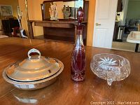 Photo showing the full set: silver-plate serving dish with lid, crystal footed bowl, and vintage red ornamental glass decanter on wooden table.