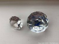 Photo showing both Swarovski crystal pieces on a white surface, highlighting their faceted design and clarity.