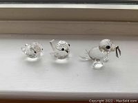 Three Swarovski crystal figurines on a white surface: two birds and one seal, all clear faceted crystal with black eyes and precise detailing.