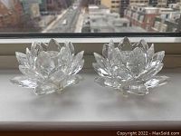 Pair of clear crystal lotus-shaped candle holders shown from above with cityscape in background.
