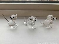 Three Swarovski animal figurines placed on a windowsill. Visible are a small poodle, a dachshund with elongated body, and a cat with a wire tail.