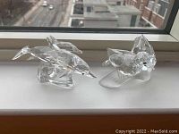 Overall view of both Swarovski crystal figurines on window ledge, showing dolphin figurine and bird figurine side by side.