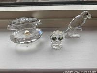 Three Swarovski crystal figurines displayed on a windowsill: oyster with pearl, owl with green eyes, and parrot.