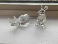 Two Swarovski crystal figurines, a rhino and a kangaroo, shown side by side on a white surface.