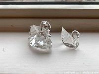 Photo of both crystal Swarovski swan figurines side by side on a white surface under natural light.