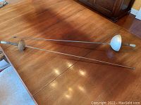Two vintage fencing foils laid out on a wooden table, showing full length and general condition.