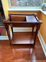 Wood magazine and newspaper rack with turned legs, open lower shelf, and sliding tray on top, showing wear.