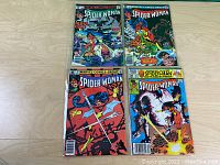 Four Marvel Comics Spider-Woman related issues displayed on a wooden table, protected in clear sleeves showing colorful covers.