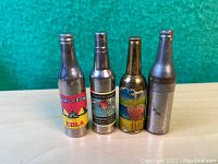 Front view of four miniature metal bottle lighters with colorful labels and bottle cap tops