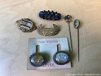 Lot of antique jewelry pieces including brooches, stickpins, and cufflinks on card, arranged on wood surface