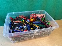 Top view showing multiple vintage diecast cars in a clear plastic bin showing variety of colors and types