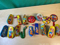 Top view of 15 vintage colorful tin noisemakers arranged on a light wood surface showing different shapes and clown/ carnival themed designs
