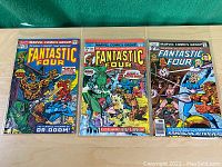 Three Fantastic Four comic book issues 143, 156, 195 with detailed colorful cover artwork showing key characters like Dr. Doom and the Silver Surfer on a wooden surface