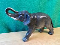 Side view of large vintage porcelain elephant figurine showing curved trunk, detailed skin texture, and dark gray glaze.