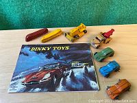 Top down photo showing all diecast vehicles and the Dinky Toys catalog on a wooden surface with a green background.