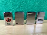 Front view of four metal Zippo lighters standing side by side showing various logos and plain designs.