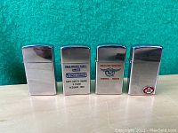 Front view of four silver-tone Zippo lighters showing plain and branded designs