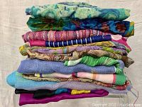 Stack of 12 folded scarves stacked on top of each other displaying variety of colors and patterns including blues, greens, purples, pinks, and multi-colors.