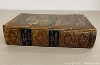 Side view of the book spine showing title and author with gold embossed text on a leather spine with decorative elements.