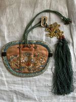 Antique embroidered silk purse on light fabric background showing full purse with green cord drawstring and tassel.